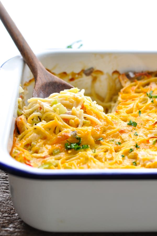 Front shot of a dish of chicken spaghetti casserole topped with cheese and fresh parsley