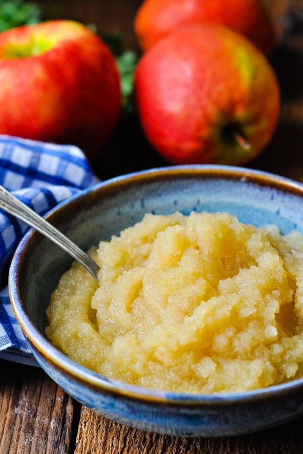 Image of a blue bowl full of homemade applesauce on a wooden table