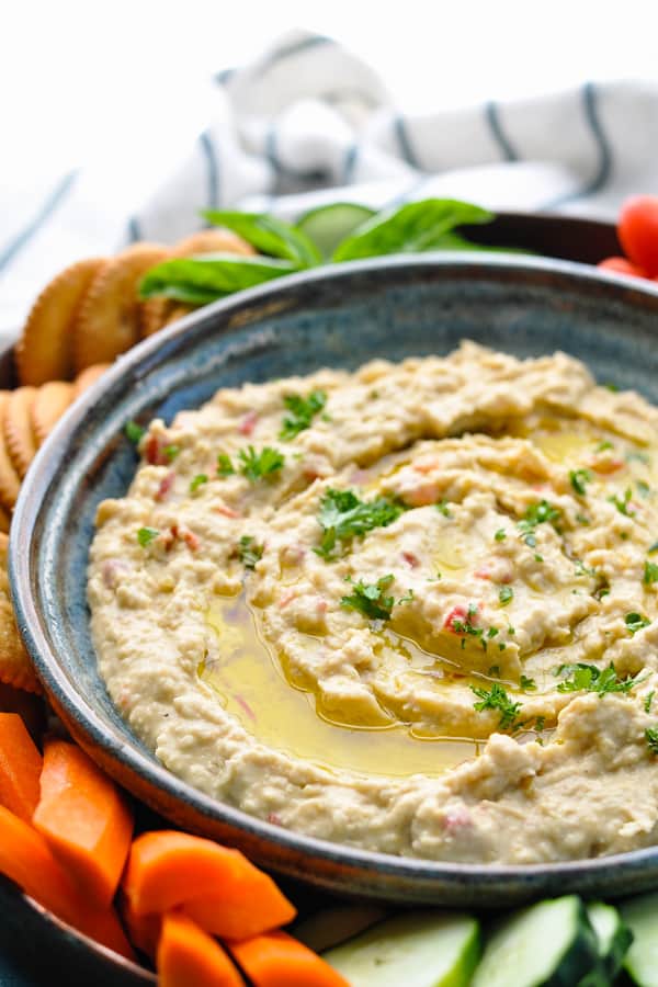 Close up front shot of a bowl of homemade hummus served with vegetables and crackers