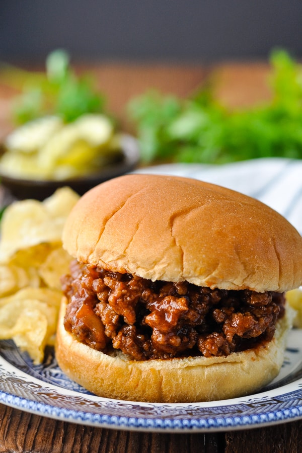 Homemade sloppy joes on a blue and white plate with potato chips on a wooden table