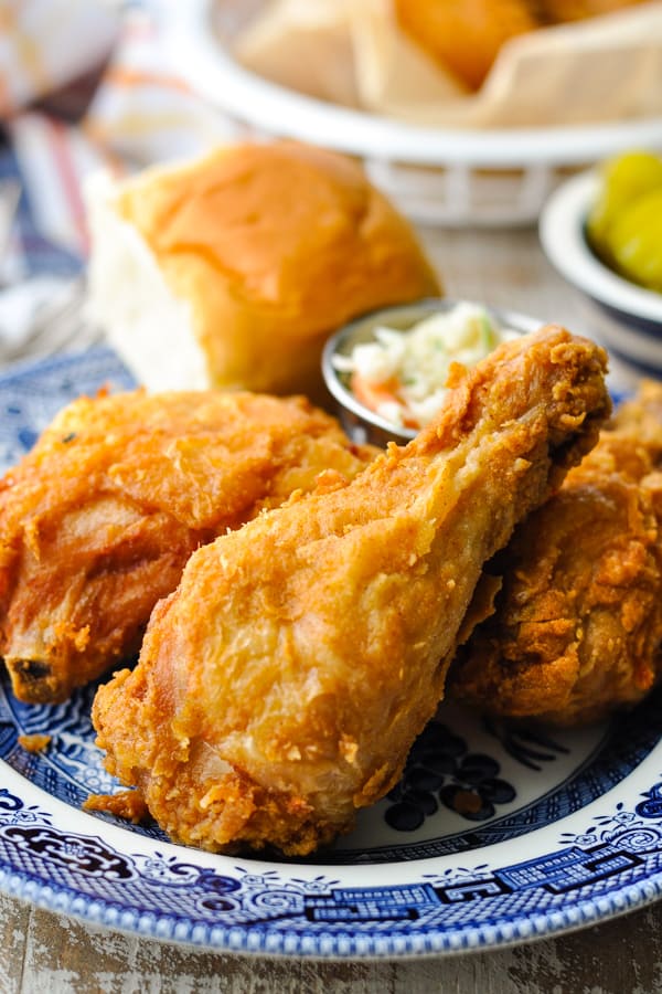 Fried chicken drumstick on a plate with coleslaw and biscuits in the background