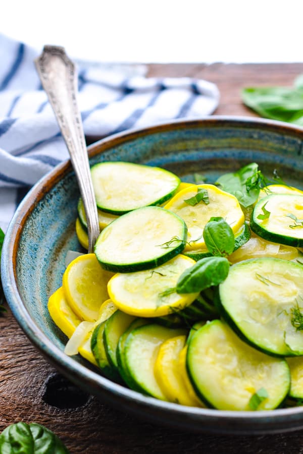 Front shot of a spoon in a bowl of sauteed zucchini with a dish towel in the background