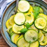 Overhead image of a blue bowl with zucchini and squash garnished with fresh basil