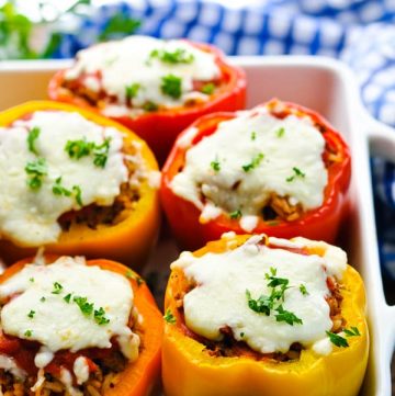 Front shot of stuffed peppers with rice and cheese in a white baking dish garnished with parsley