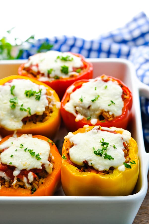 Front shot of stuffed peppers with rice and cheese in a white baking dish garnished with parsley