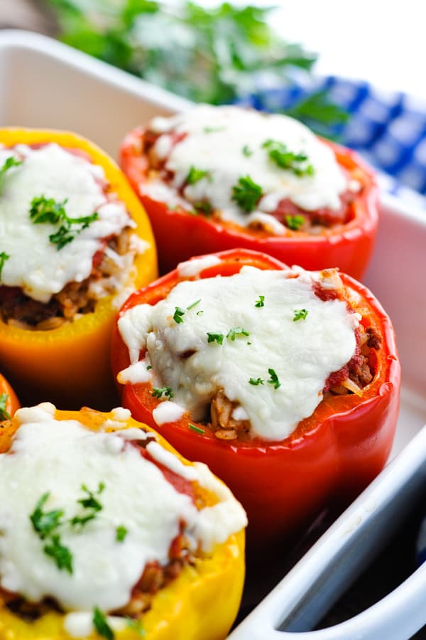 Close up side shot of stuffed peppers with rice and mozzarella in a white dish topped with fresh parsley