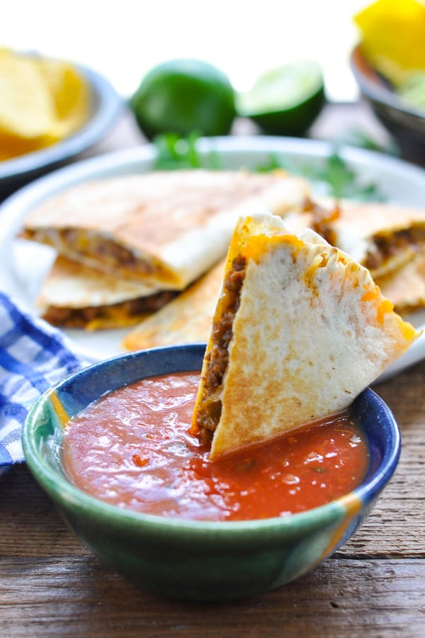 Front shot of a cheesy ground beef quesadilla dipping in a bowl of salsa