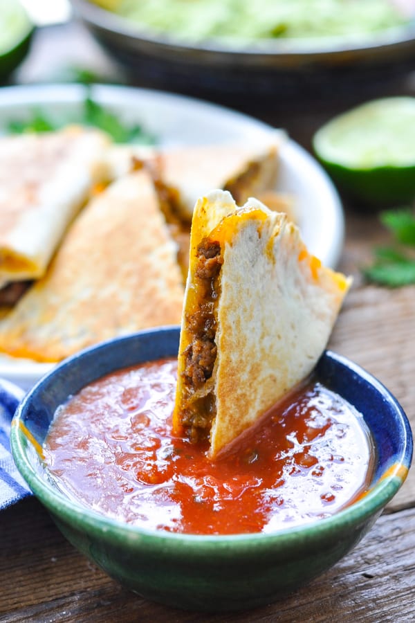 Close up shot of ground beef quesadilla in a bowl of salsa