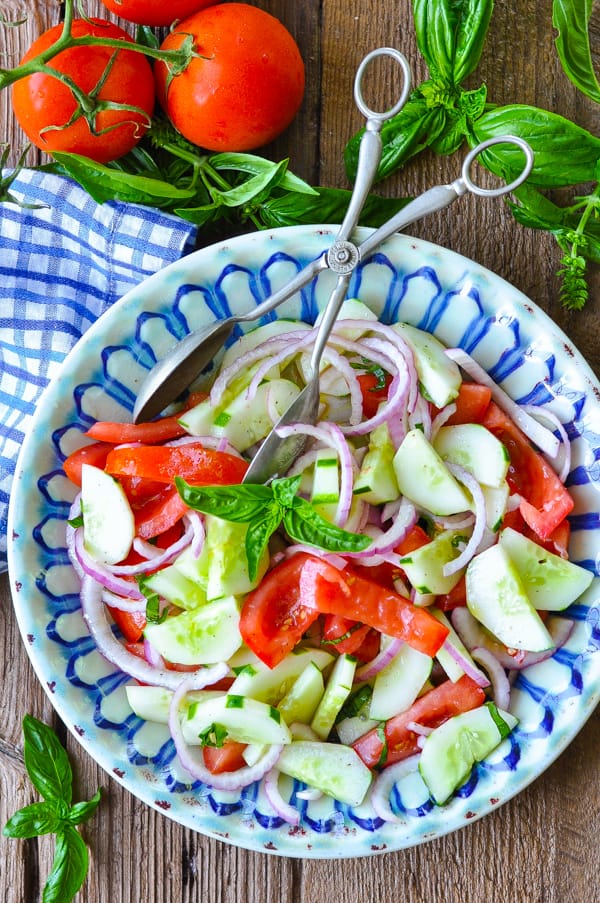 Overhead shot of a bowl of tomato cucumber salad with onion and fresh basil