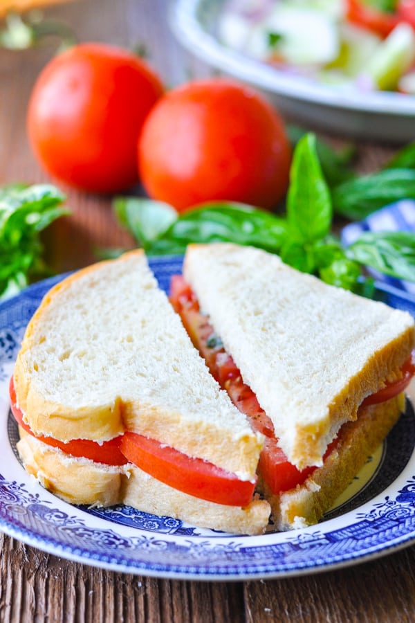 Close up side shot of a tomato sandwich with basil on white bread