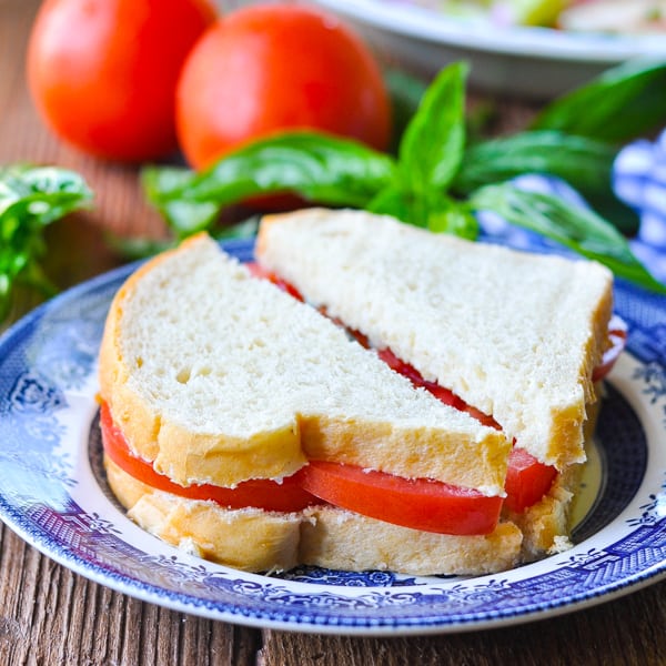 Square image of a tomato sandwich on a blue and white plate