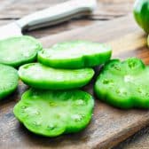 Sliced green tomatoes on a wooden cutting board.