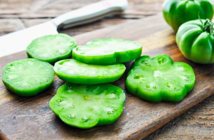 Sliced green tomatoes on a wooden cutting board.