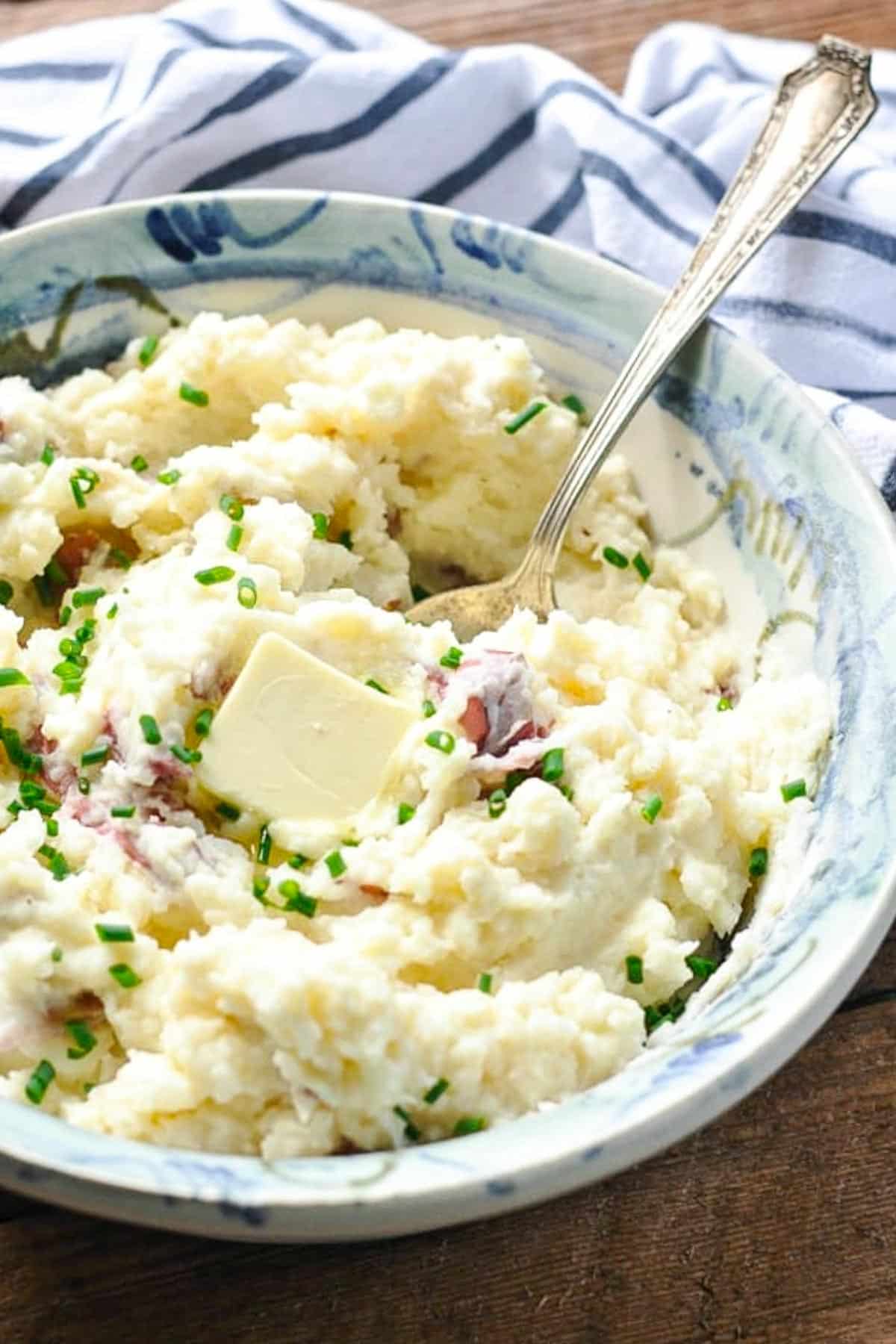 Close up side shot of skin on mashed red potatoes in a bowl with butter and chives.