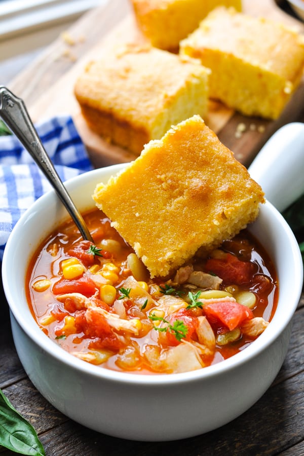 Front shot of a bowl of brunswick stew with a piece of cornbread on the side