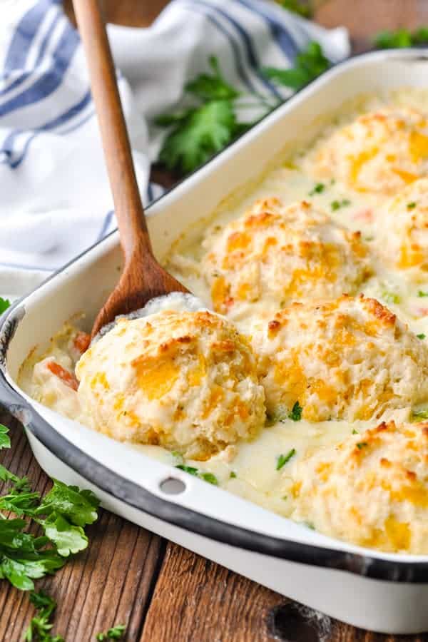 Wooden spoon serving chicken and biscuits from a white casserole dish