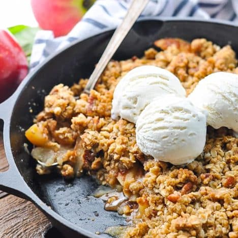 Square close up side shot of an easy apple crisp recipe in a cast iron skillet with vanilla ice cream on top.