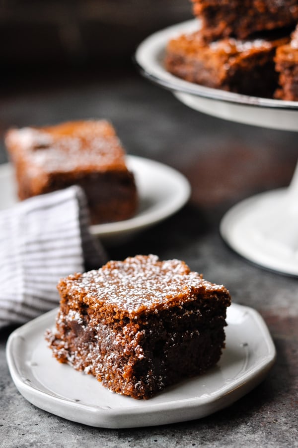 Close up shot of a moist chewy fudgy brownie on a small plate with powdered sugar on top