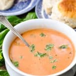 Close up shot of a bowl full of roasted tomato basil soup with biscuits in the background
