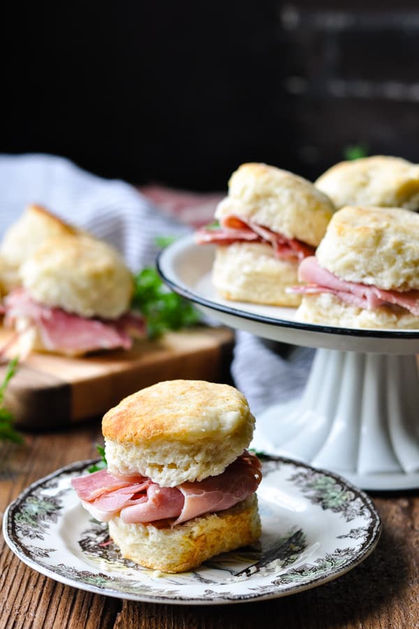 Front shot of a small plate of country ham biscuits with a larger serving tray in the background
