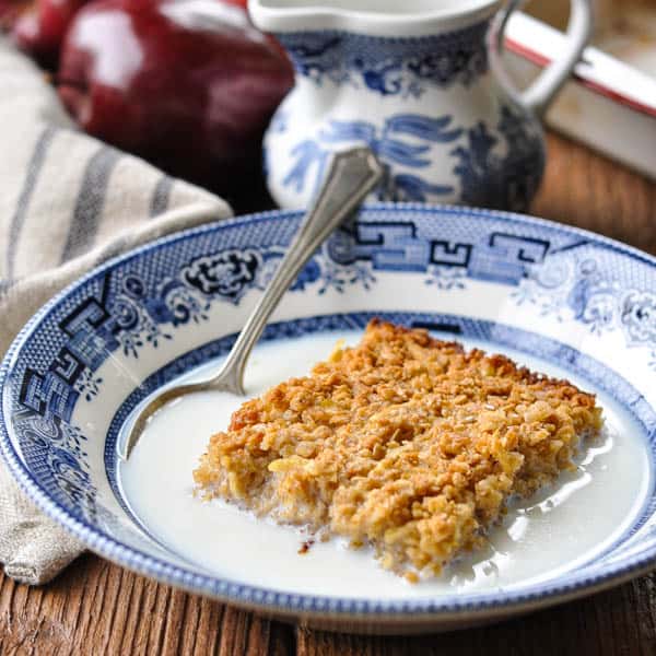 Square image of a bowl of amish baked oatmeal with milk and apples in the background