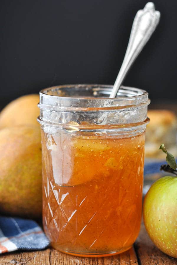 Jar of spiced pear jam with apples on a wooden table