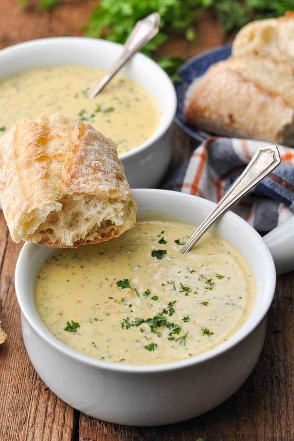 Front shot of a bowl full of the best broccoli cheese soup recipe with baguette