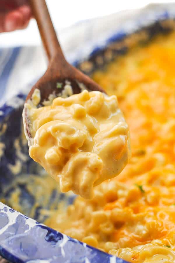 Wooden spoon serving creamy mac and cheese from a dish