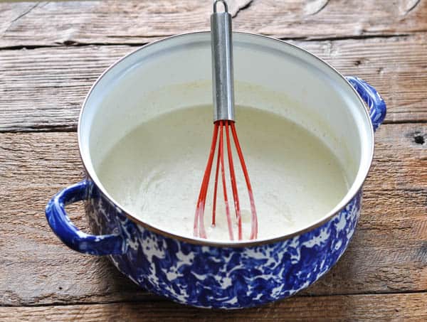 Creamy white sauce in a blue and white dutch oven with whisk