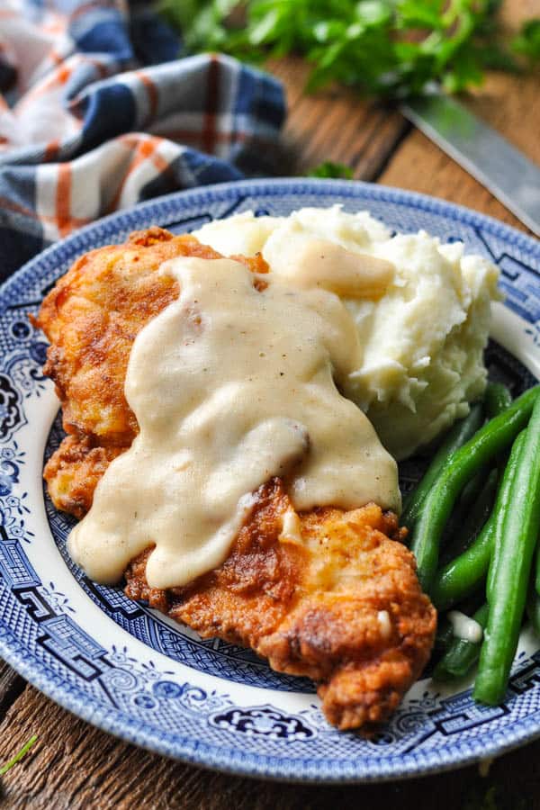 Front shot of crispy pan fried chicken cutlets on a plate with mashed potatoes and gravy