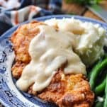Fried chicken and gravy on a blue and white plate smothered in gravy