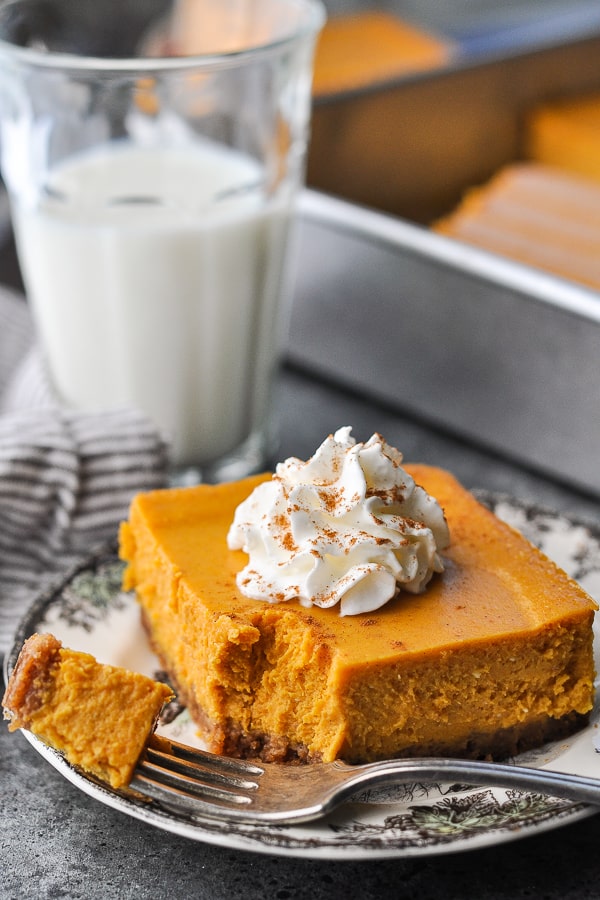 Front shot of a pumpkin cheesecake bar with a bite taken out of it on a plate