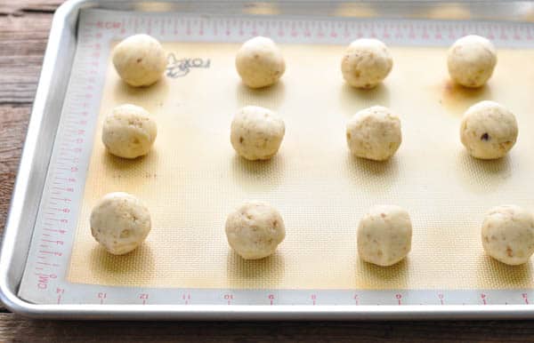 Small, round, unbaked Russian tea cake cookies lined up on a silicone-lined baking sheet.