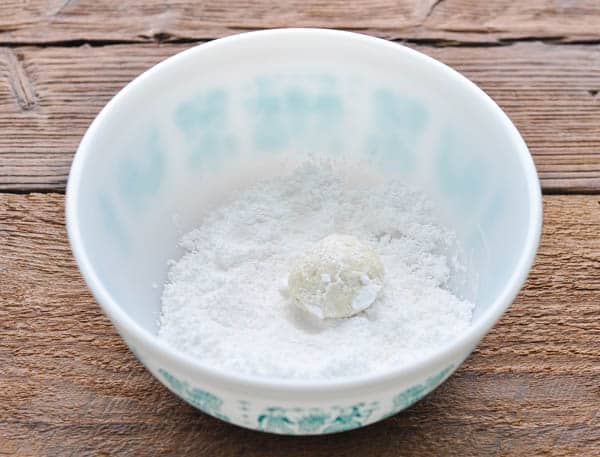 A small Russian tea cake cookie rolled in a bowl of powdered sugar.