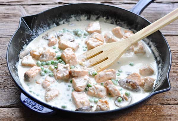 Salmon pasta cream sauce in a cast iron skillet with a wooden spoon