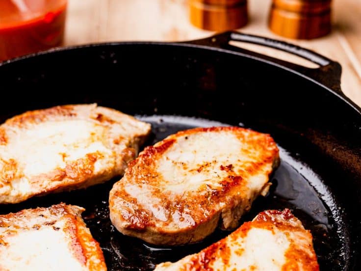 Browning pork chops in a cast iron skillet before slow cooking.