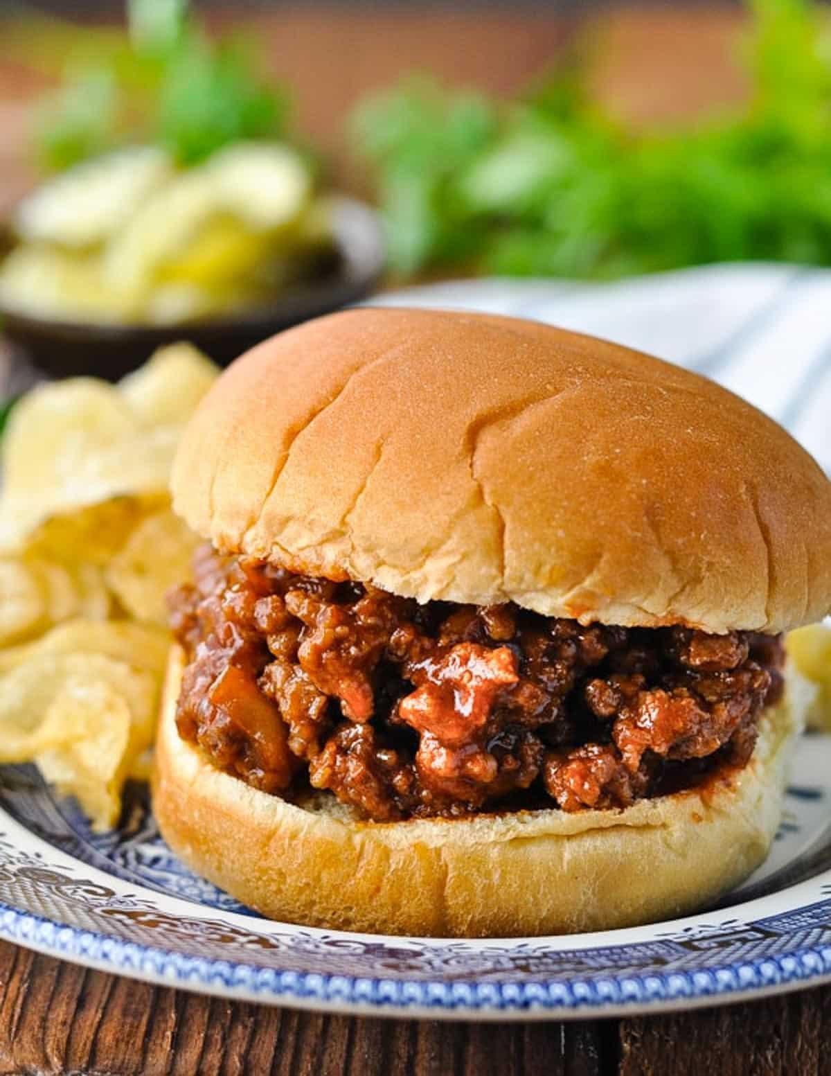 Close up side shot of the best old fashioned sloppy joes recipe served on a bun with potato chips on the side.