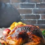 A beautiful roasted turkey flavored with an apple cider turkey brine on a platter in front of a dark brick wall