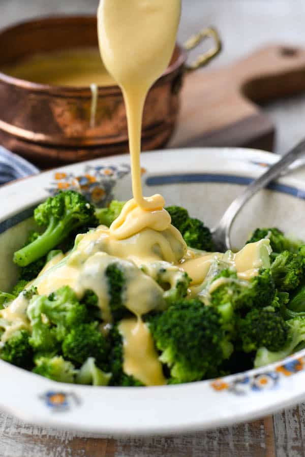 Pouring cheese sauce on top of steamed broccoli