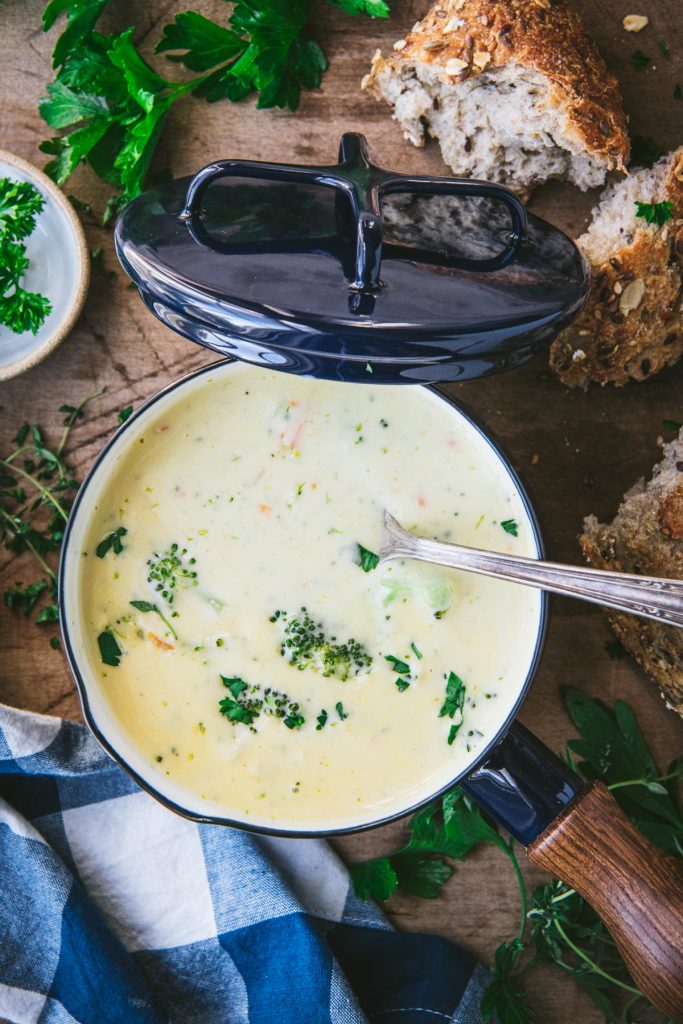 Overhead shot of a spoon in a blue pot of broccoli and cheese soup