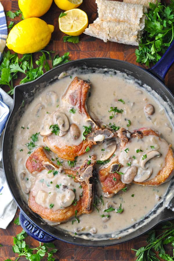 Pork chops with creamy mushroom sauce recipe in a cast iron skillet with fresh parsley on top