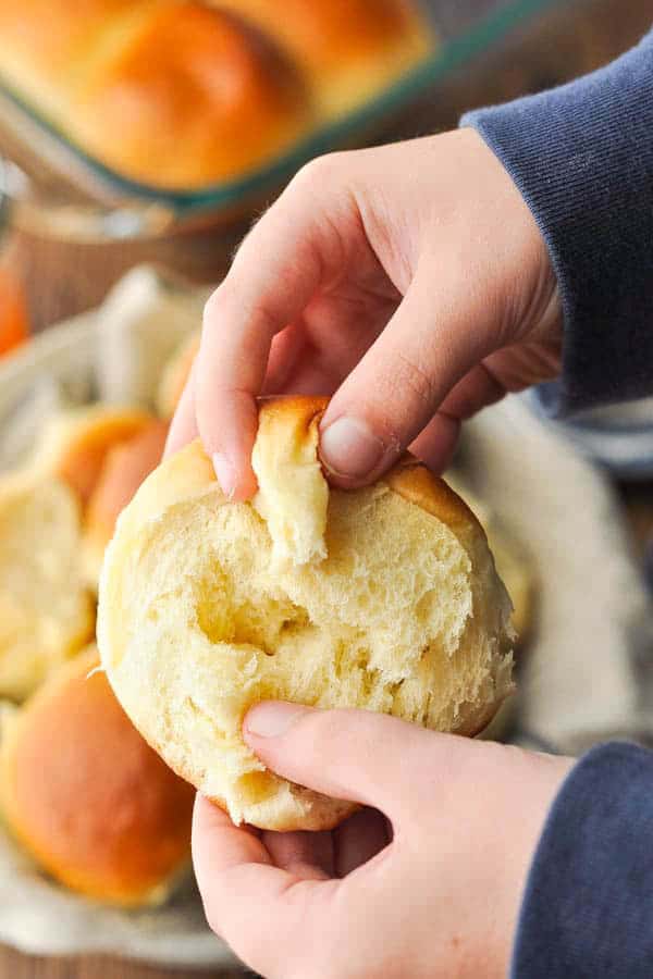 Hands pulling apart a soft dinner roll