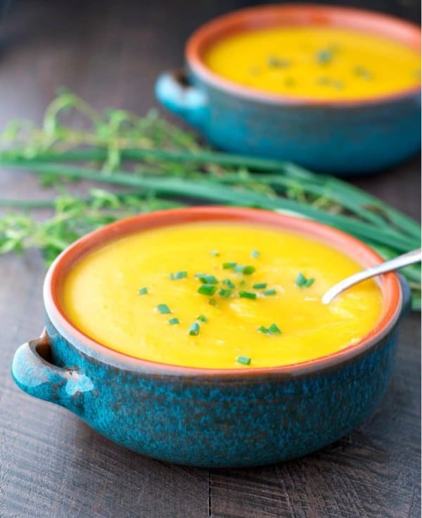 Two bowls of roasted butternut squash soup on a table with fresh chives