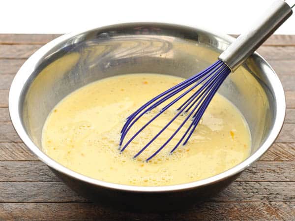 Egg custard mixture in a metal bowl with blue whisk
