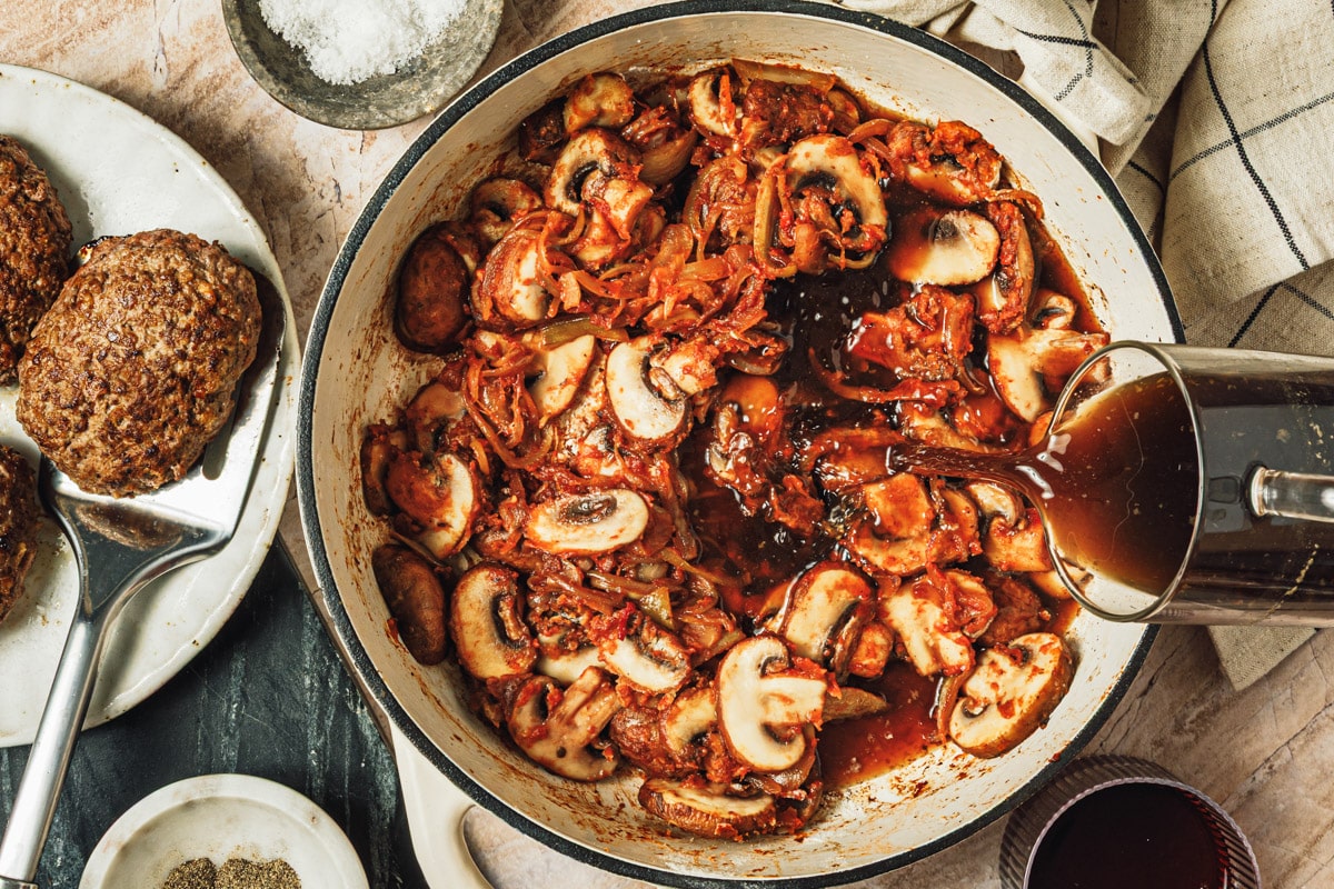 Adding the red wine and broth to a pan of mushroom gravy.