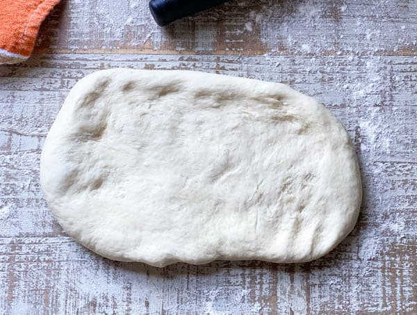 A rectangle of raw baguette dough rolled out on a floured work surface.