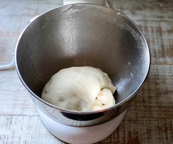 A smooth, round ball of baguette dough sits in a metal stand mixer bowl.