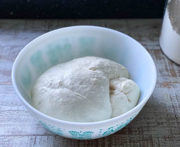 A bowl full of puffed up, proofed baguette dough in a white and green patterned bowl.