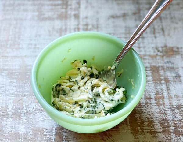 Softened butter in a small green bowl with garlic and herbs