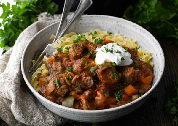 Horizontal shot of traditional hungarian goulash in a ceramic bowl with noodles and sour cream